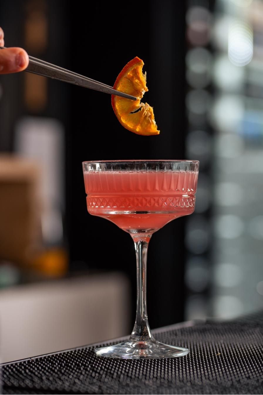 Coppa con cocktail rosa e guarnizione di arancia al bar